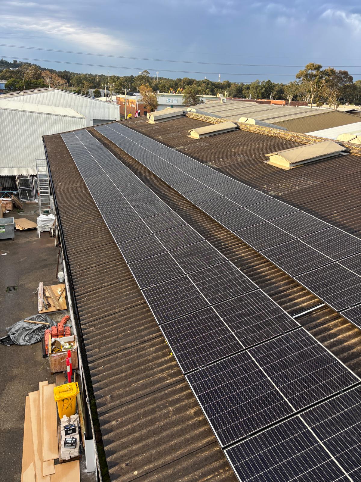 Long rows of solar panels down a corrugated industrial roof, clear of the skylights.